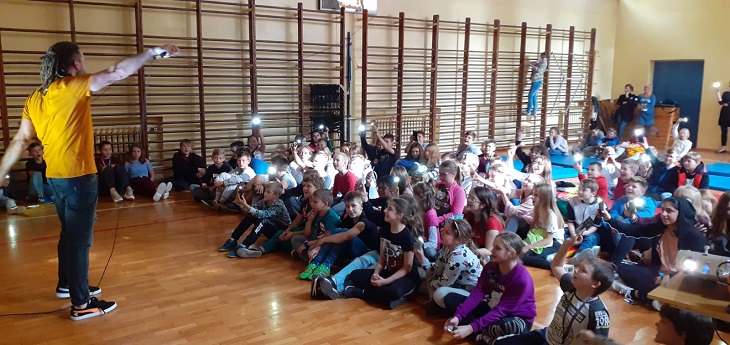 Artysta ma skierowany mikrofon w stronę dzieci. dzieci siedzą na podłodze i słuchają