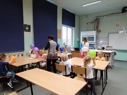 Dzieci w sali fizycznej siedzą przy stołach z balonami