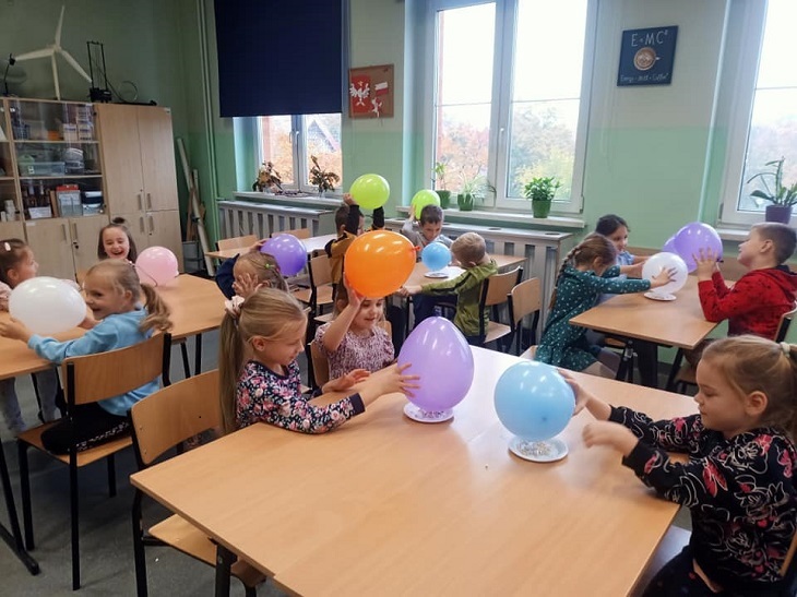 Dzieci siedzą w sali fizycznej. W rękach trzymają balony. 