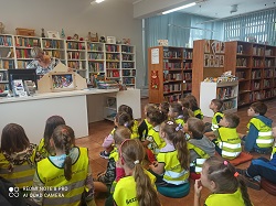 Dzieci siedzą w bibliotece i oglądają tetarzyk