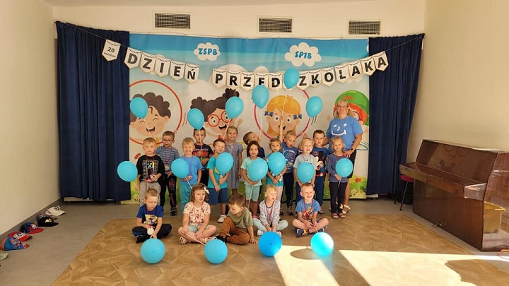 Dzieci ubrane na niebiesko pozują do zdjęcia. na ziemi leżą niebieskie balony