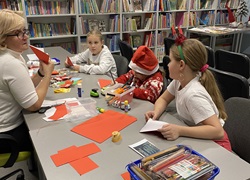 nauczycielka z dziećmi siedzi w bibliotece szkoplnej pokazuje im obrazki, dziewczinki sa zainteresowane, impreza z okazji kiermaszu świątecznego