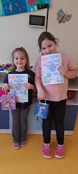 Za zdjęciu dwie dziewczynki prezentują swoje dyplomy i nagrody za osiągniecia w konkursie plastycznym
