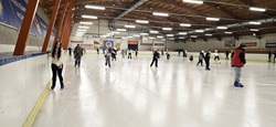 Na zdjęciu widać dużą halę lodowiska, na którego tafli jednocześnie jeździ wiele osób. Uczniowie poruszają się po lodzie w różnych kierunkach, część z nich jeździ samodzielnie, inni w mniejszych grupach. Widoczna jest aktywność i ruch, a cała scena oddaje atmosferę wspólnej zabawy oraz sportowego wysiłku. Lodowisko jest przestronne i dobrze oświetlone, a bandy oraz konstrukcja hali wskazują na obiekt miejski przystosowany do zajęć rekreacyjnych. Zdjęcie pokazuje radosny, aktywny charakter wyjścia szkolnego i czas spędzony na świeżej aktywności.