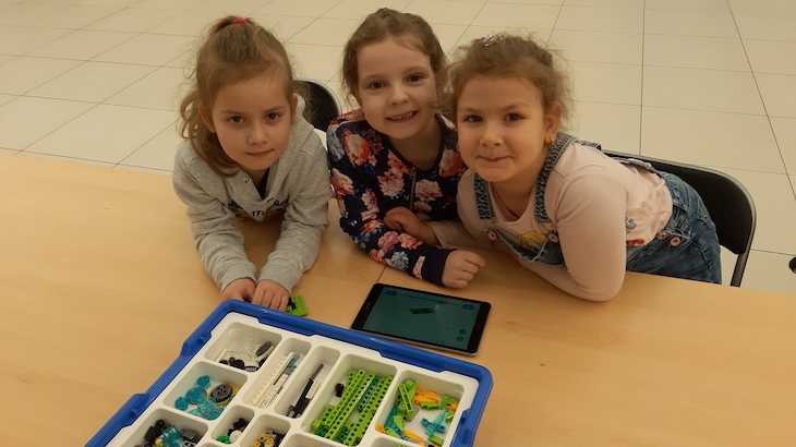 trzy dziewczynki budują robota z klocków zgodnie z instrukcją na tablecie