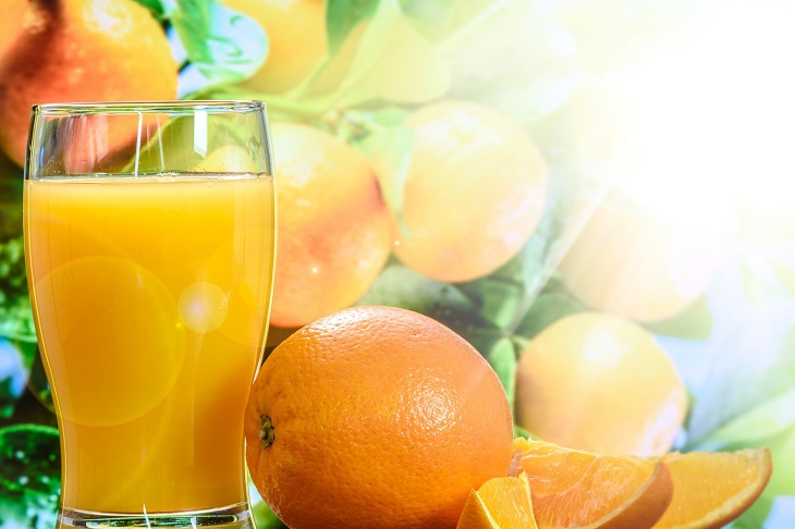 sok pomarańczowy w szklance obok pomarańcza