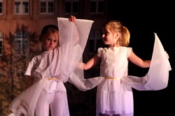 Dziewczynki na scenie tańczą w przebraniu aniołków. W rękach trzymają białe szarfy.