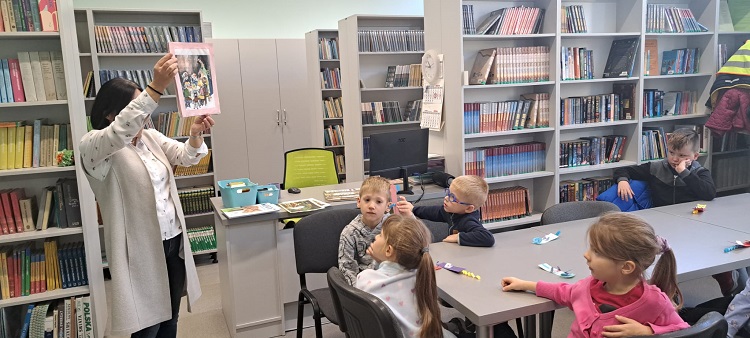 Bibliotekarka w bibliotece pokazuje dzieciom książki, lekcja biblioteczna