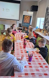 Na zdjęciu dzieci siedzą przy stole i zajmują się kolorowaniem otrzymanych obrazków. W tle znajduje się włączony rzutnik.