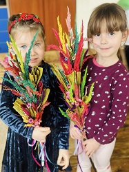 na zdjęciu dwie dziewczynki trzymają w rękach piękne kolorowe palmy wielkanocne