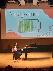 na zdjęciu sala koncertowa szkoły muzycznej, w tle dziecko gra na flecie poprzeczny, a dorosła osoba akompaniuje na fortepianie