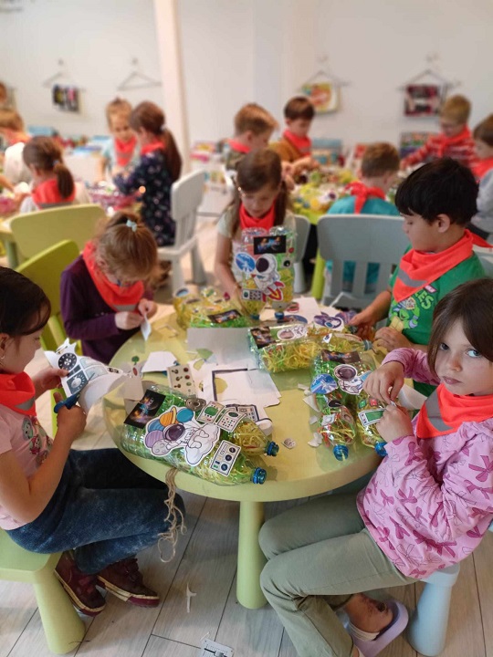 na zdjęciu dzieci siedzą dookoła stolików i robią ekozabawki z plastikowych butelek