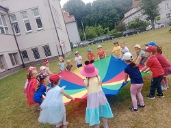 na zdjęciu grupa dzieci stoi dookoła chusty animacyjnej w przedszkolnym ogrodzie