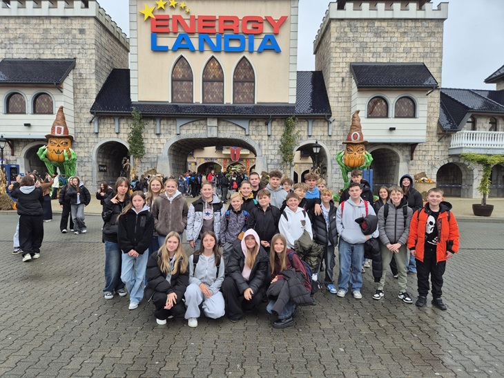 Na zdjęciu znajduje się grupa uczniów pozujących przed wejściem do Parku Rozrywki Energylandia w Zatorze. W tle widać charakterystyczną bramę z dużym napisem ENERGYLANDIA oraz dekoracje w bajkowym stylu. Uczniowie są ciepło ubrani, co wskazuje, że wycieczka odbyła się w chłodniejszy dzień.