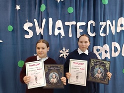 dwie dziewczynki stoją i trzymają dyplomy oraz książki, wygrany konkurs