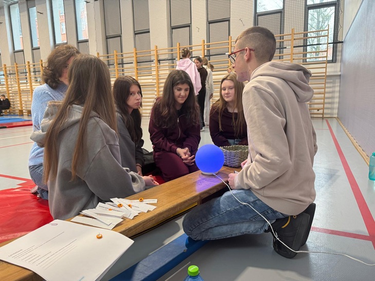 mężczyzna i kilka dziewczyn klęczą w sali gimnastycznej, rozmawiają o ważnych sprawach, warsztaty profilaktyczne