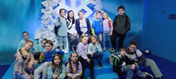 Na zdjęciu widać grupę dzieci wraz z opiekunkami, pozujących do wspólnej fotografii w Funzeum. Tło zdjęcia jest niebieskie, ozdobione białymi, sztucznymi drzewkami i dużym symbolem śnieżynki, co tworzy zimową, bajkową scenerię