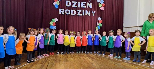 grupa uśmiechniętych dzieci na występie ubrane w kolorowe fartuszki i stroje
