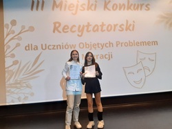 uczennice biorace udział w konkursie recytatorskim na tle napisu Konkurs recytatorski