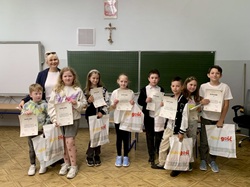 Na zdjęciu widzimy uczestników konkursu „Mistrz savoir-vivre’u”, o którym mowa w poprzednim tekście.  Uczniowie klas trzecich stoją w sali lekcyjnej, dumnie prezentując swoje dyplomy oraz nagrody za udział w konkursie. Towarzyszy im nauczycielka – najprawdopodobniej organizatorka wydarzenia. Dzieci ubrane są swobodnie, a na ich twarzach widać radość i satysfakcję z udziału w wydarzeniu. 