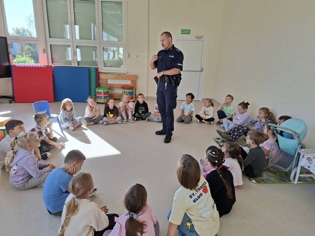 dzieci siedzą w kręgu, nad nimi stoi policjant w mundurze