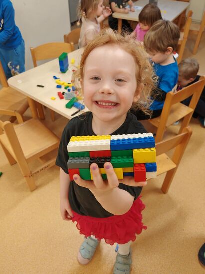 dziewczynka uśmiechnięta trzymająca budowlę z klocków lego