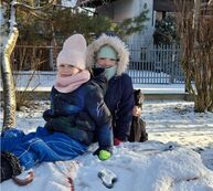 uśmiechięte dziewczynki siedzące na śniegu w zimowych kombinezonach
