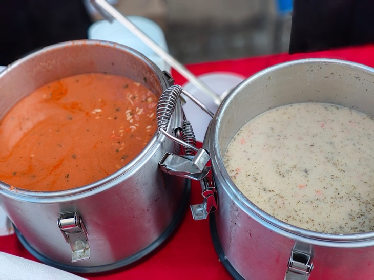 Na zdjęciu widzimy dwa duże termosy gastronomiczne wypełnione gorącymi potrawami – pomidorową zupą oraz jasną zupą z dodatkami. Przygotowany poczęstunek jest przykładem wsparcia i solidarności z osobami potrzebującymi. Takie inicjatywy pokazują, jak ważne są empatia, dzielenie się z innymi i niesienie pomocy tym, którzy jej potrzebują