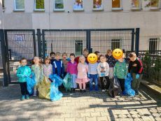 grupa dzieci stojąca przed przedszkolem z workami w rękach, gotowe do sprzątania