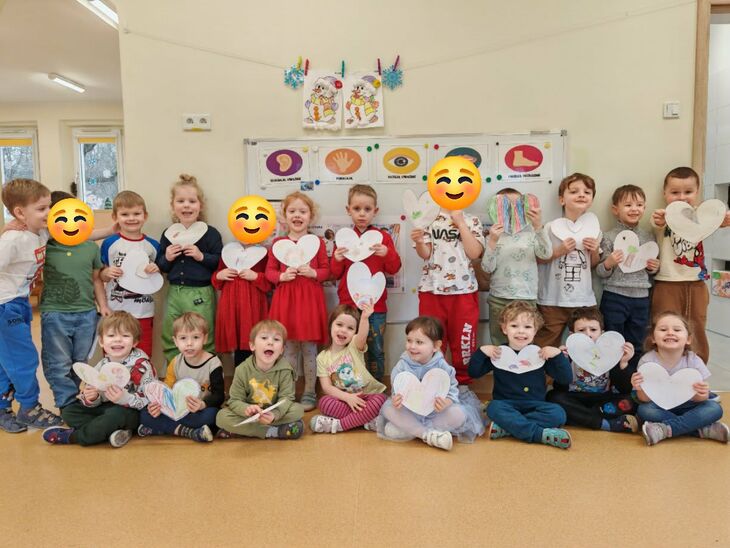 grupa uśmiechniętych dzieci stojących pod ścianą z rysunkami serduszek w rękach