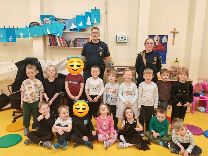 uśmiechnięte dzieci stojące przed dwójką strażników miejskich ubranych w mundury