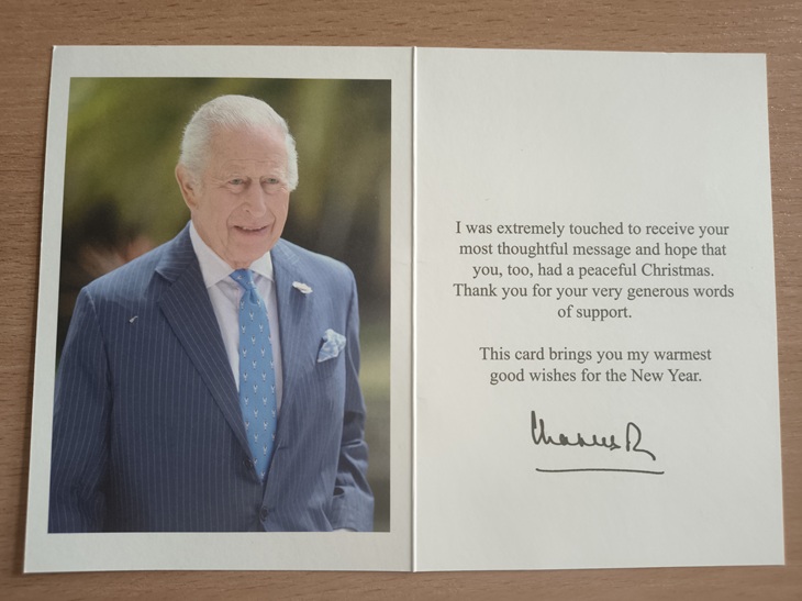 Na zdjęciu widać otwartą kartkę z życzeniami. Po lewej stronie znajduje się oficjalna fotografia króla Karola III, a po prawej wydrukowana wiadomość z podziękowaniem za list oraz życzeniami na Nowy Rok, zakończona odręcznym podpisem „Charles R”.