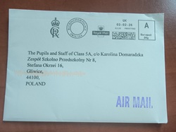Na zdjęciu widać kopertę przesyłki lotniczej („Air Mail”) wysłanej z Wielkiej Brytanii do Szkoły Podstawowej nr 8 im. Stefana Okrzei w Gliwicach. W lewym górnym rogu znajduje się oznaczenie nadawcy z Pałacu Buckingham, a na kopercie widoczny jest także królewski herb oraz data nadania.