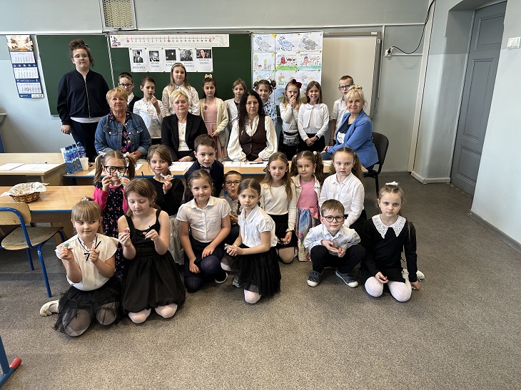 Uczniowie i nauczyciele siedzą, pozują do zdjęcia w sali lekcyjnej