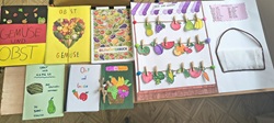 Na zdjęciu widać kolorowe prace uczniów przygotowane na konkurs – słowniczki obrazkowe dotyczące owoców i warzyw. Każda praca jest wykonana starannie i kreatywnie, z wykorzystaniem rysunków, wycinanek oraz różnych materiałów. Szczególnie wyróżnia się makieta z przypiętymi obrazkami owoców i warzyw, przypominająca mały stragan.