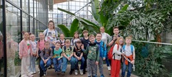 Grupa uczniów wraz z opiekunami pozuje do wspólnego zdjęcia w Egzotarium, otoczona bujną, zieloną roślinnością. Wszyscy są uśmiechnięci, co podkreśla radosną atmosferę wycieczki.