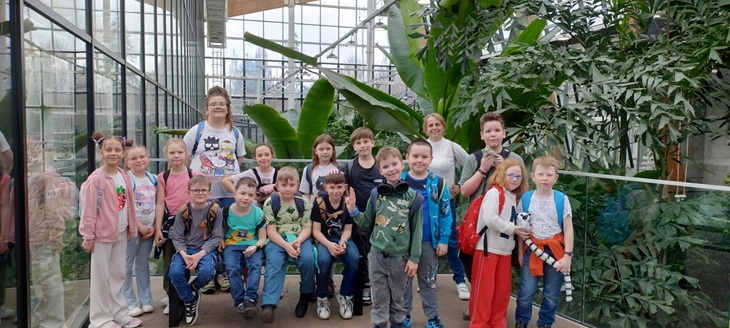 Grupa uczniów wraz z opiekunami pozuje do wspólnego zdjęcia w Egzotarium, otoczona bujną, zieloną roślinnością. Wszyscy są uśmiechnięci, co podkreśla radosną atmosferę wycieczki.