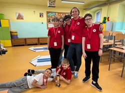 Drużyna wraz z opiekunem prezentuje zdobyty puchar po zawodach z pierwszej pomocy. Uczniowie w czerwonych koszulkach z dumą świętują swój sukces.