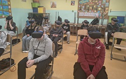 Uczniowie siedzą w klasie w ławkach, mają na głowach gogle VR i uczestniczą w wirtualnych zajęciach. W skupieniu „przenoszą się” do cyfrowego świata, doświadczając lekcji w nowoczesny i angażujący sposób.