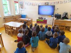 grupa dzieci siedząca przed ekranem, oglądająca prezentację o autyzmie