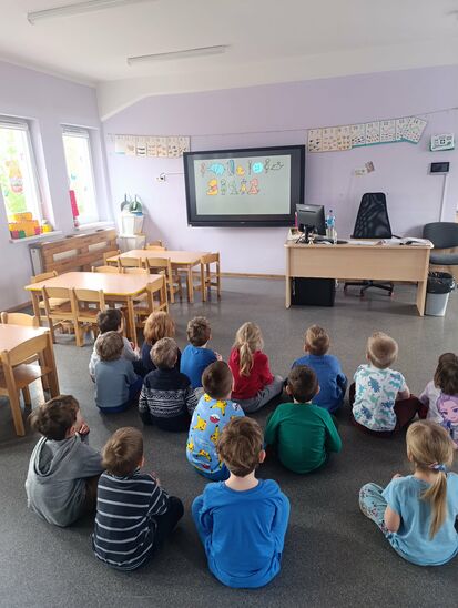 grupa dzieci siedząca przed ekranem, oglądająca prezentację o autyzmie