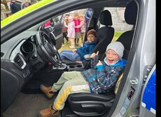 dwójka chłopców uśmiechniętych siedząca w radiowozie policyjnym