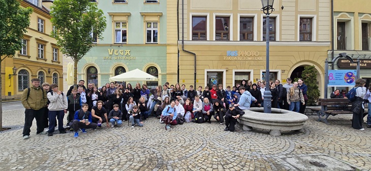 Na zdjęciu widać uczestników wycieczki klas 6 podczas pobytu we Wrocławiu. Uczniowie wraz z opiekunami pozują do wspólnego zdjęcia na rynku otoczonym kolorowymi kamienicami. Większość grupy uśmiecha się do aparatu, co pokazuje dobrą atmosferę i radość ze wspólnie spędzonego czasu.  W tle można dostrzec zabytkową zabudowę oraz klimatyczne uliczki Wrocławia, które podkreślają wyjątkowy charakter miasta. To pamiątkowe zdjęcie doskonale oddaje atmosferę wyjazdu pełnego atrakcji, integracji i wspólnych przeżyć.