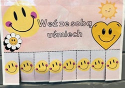 Na zdjęciu widać cztery kolorowe kartki/plakaty z krótkimi, pozytywnymi hasłami, przymocowane w różnych miejscach.  Lewy górny: pastelowa kartka z uśmiechniętymi buźkami i kwiatkiem. Główne hasło: „Weź ze sobą uśmiech”. Na dole znajdują się odrywane paski z powtarzającymi się uśmiechniętymi buźkami. Prawy górny: niebieska kartka z ilustracją osoby trzymającej serce. Hasło: „Weź ze sobą słowo, które jest Ci potrzebne”. Na dole są odrywane paski z różnymi pozytywnymi słowami, m.in. „szacunek”, „zrozumienie”, „cierpliwość” i „wdzięczność”. Lewy dolny: kartka z niebiesko-zielonym akwarelowym tłem. Napis: „Weź to, czego potrzebujesz”. Poniżej znajdują się odrywane paski z nazwami różnych potrzeb/wartości. Prawy dolny: kolejna wersja kartki z hasłem „Weź ze sobą słowo, które jest Ci potrzebne”, tym razem z ilustracją dwóch osób. Również posiada odrywane paski z pozytywnymi słowami.  Całość ma ciepły, wspierający i motywacyjny charakter – zachęca przechodniów, żeby oderwali wybrane słowo lub hasło i zabrali je ze sobą.