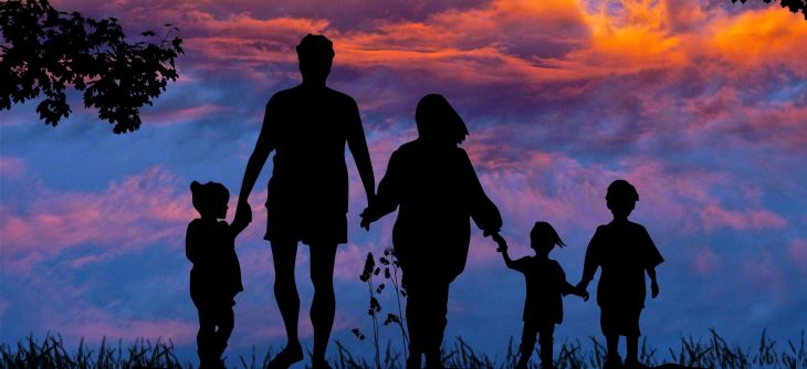 Na tle fioletowego nieba idzie rodzina, której członkowie trzymają się za ręce. W kolejności dziecko, mężczyzna, kobieta, dziecko i dziecko